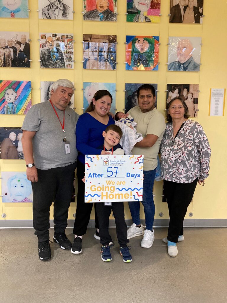 A family stands around a sign that says "Going Home after 57 days"